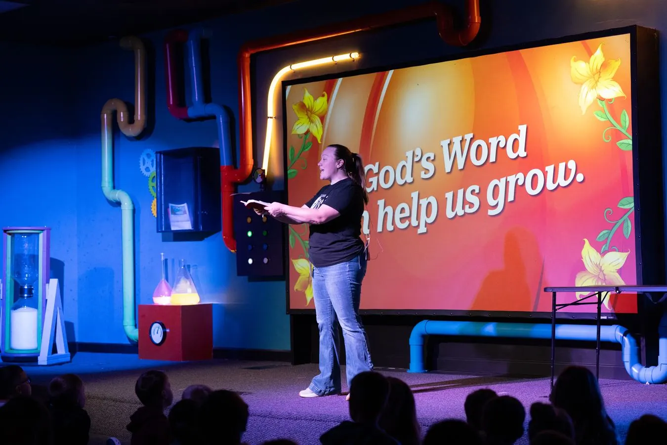 A Southland Kids leader reading from the Bible on stage in front of a screen that says God’s Word helps us grow