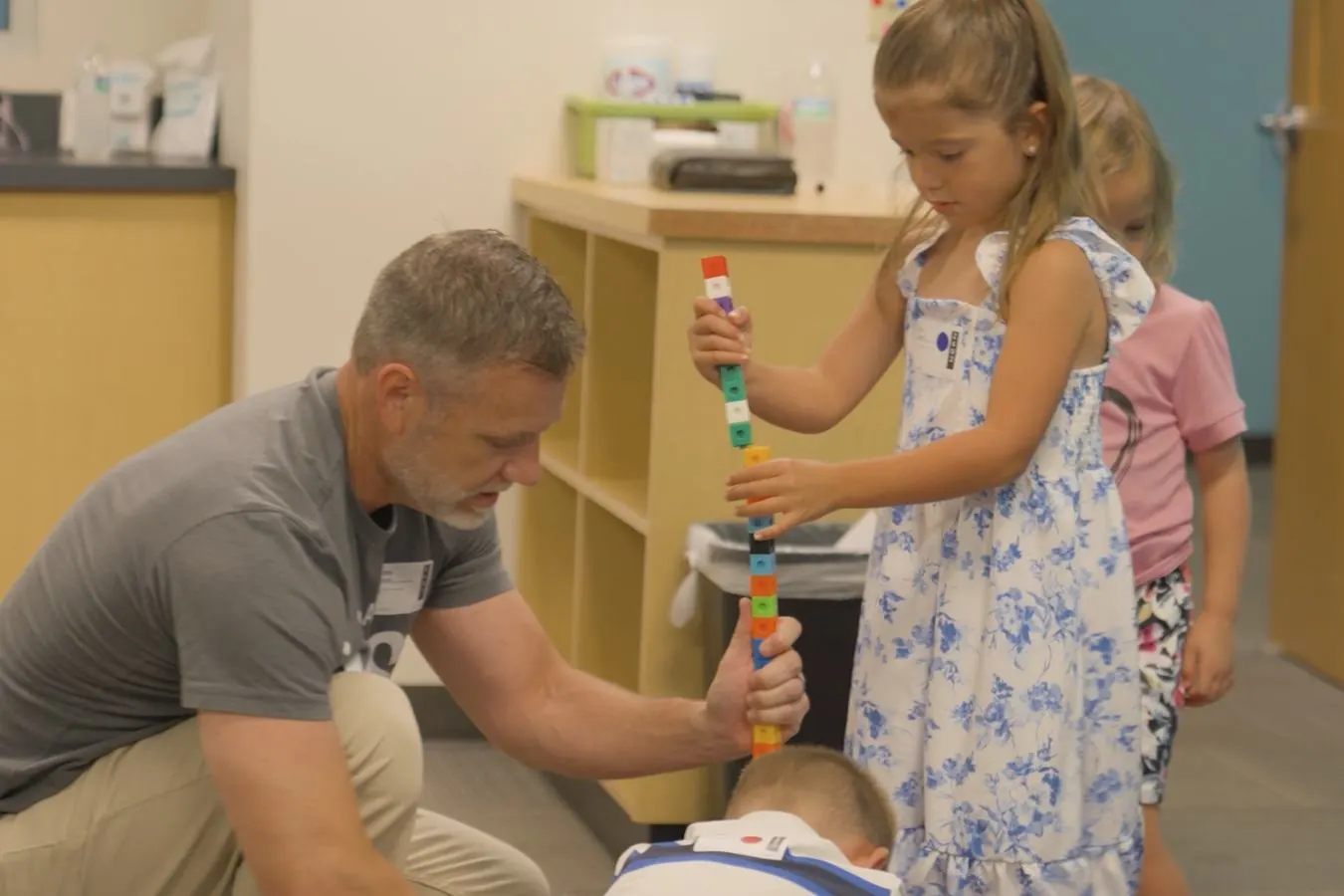 A leader kneeling with kids as they build a tower of blocks in a classroom