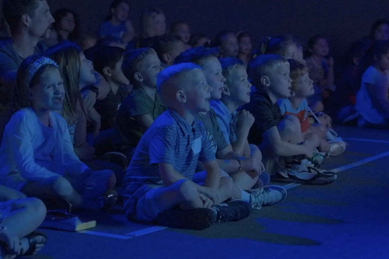 Kids sitting on the floor, smiling and watching the stage in Southland Kids