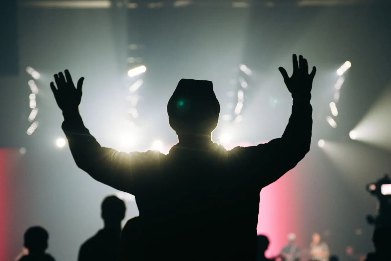 A silhouetted student with both hands raised in worship